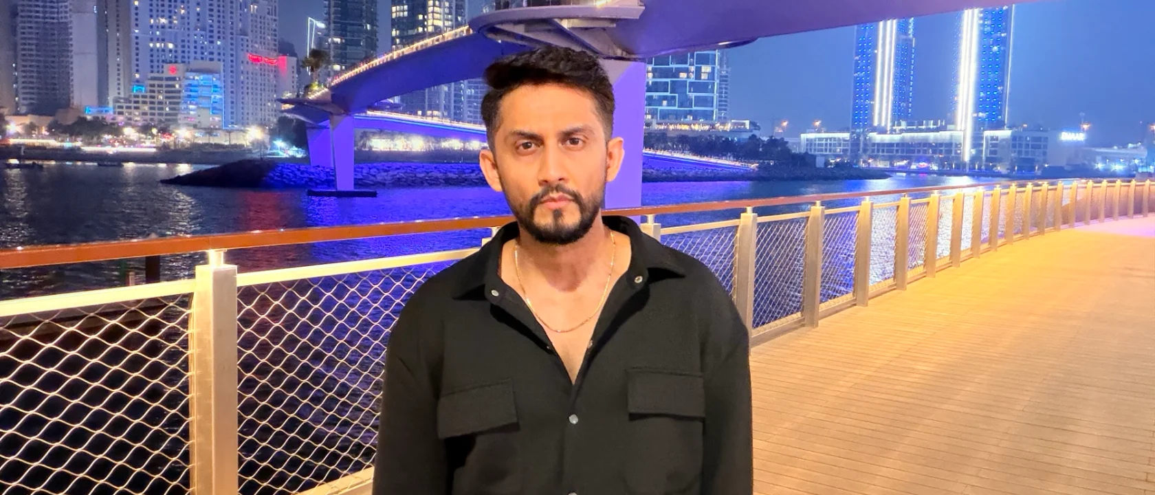 Digital Pratik, man standing on a dubai waterfront boardwalk at night, looking straight at the camera