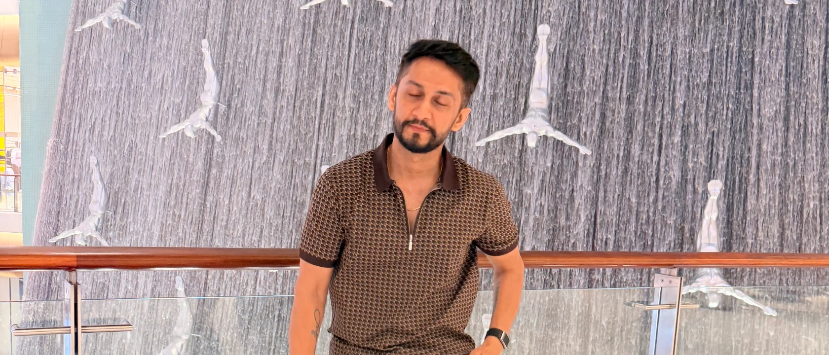 Digital Pratik, close-up of man's smiling face and neck, a wrist tattoo reading "JORRPARIVAR" visible, near the waterfall