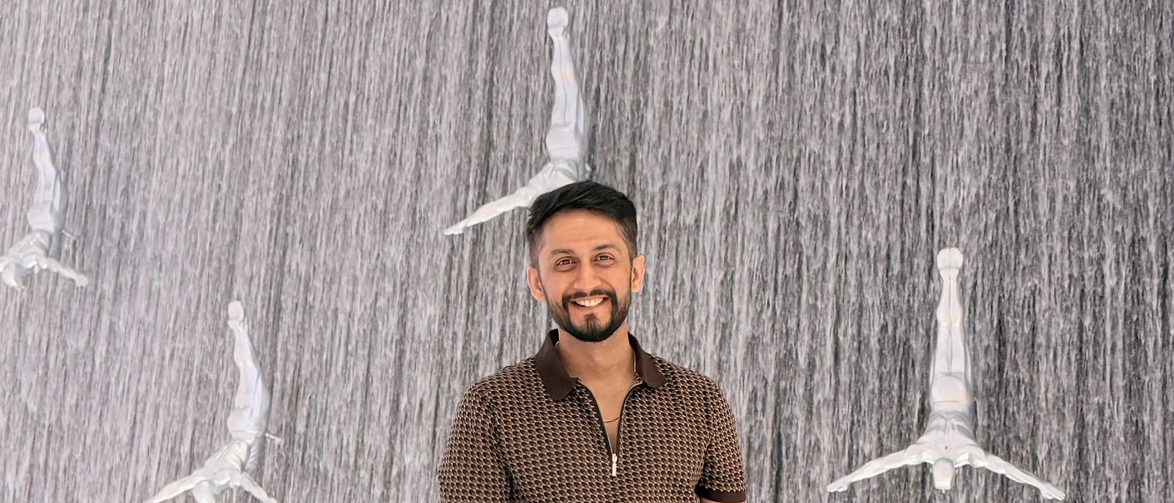 Digital Pratik smiling in front of a big indoor waterfall wall with white diver statues