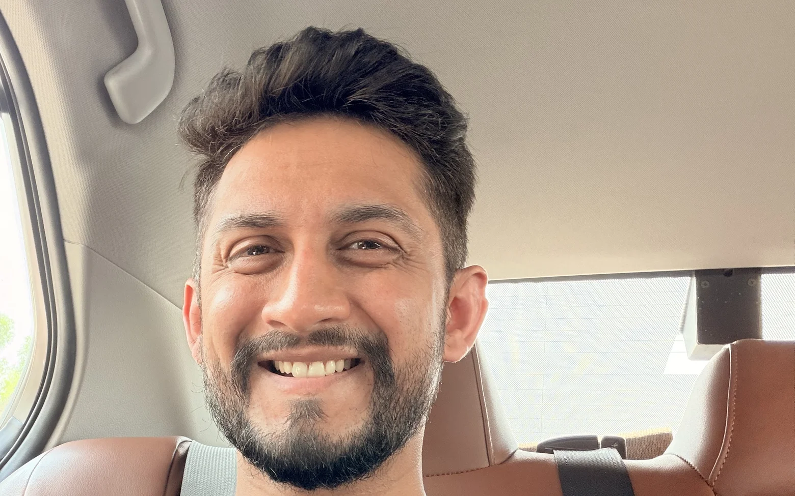 Digital Pratik smiling wide in a car selfie, his seat belt on