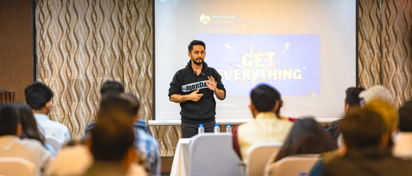 Digital Pratik on stage at his March 2024 workshop in a black JorrDaar hoodie, a room of people watching from their chairs