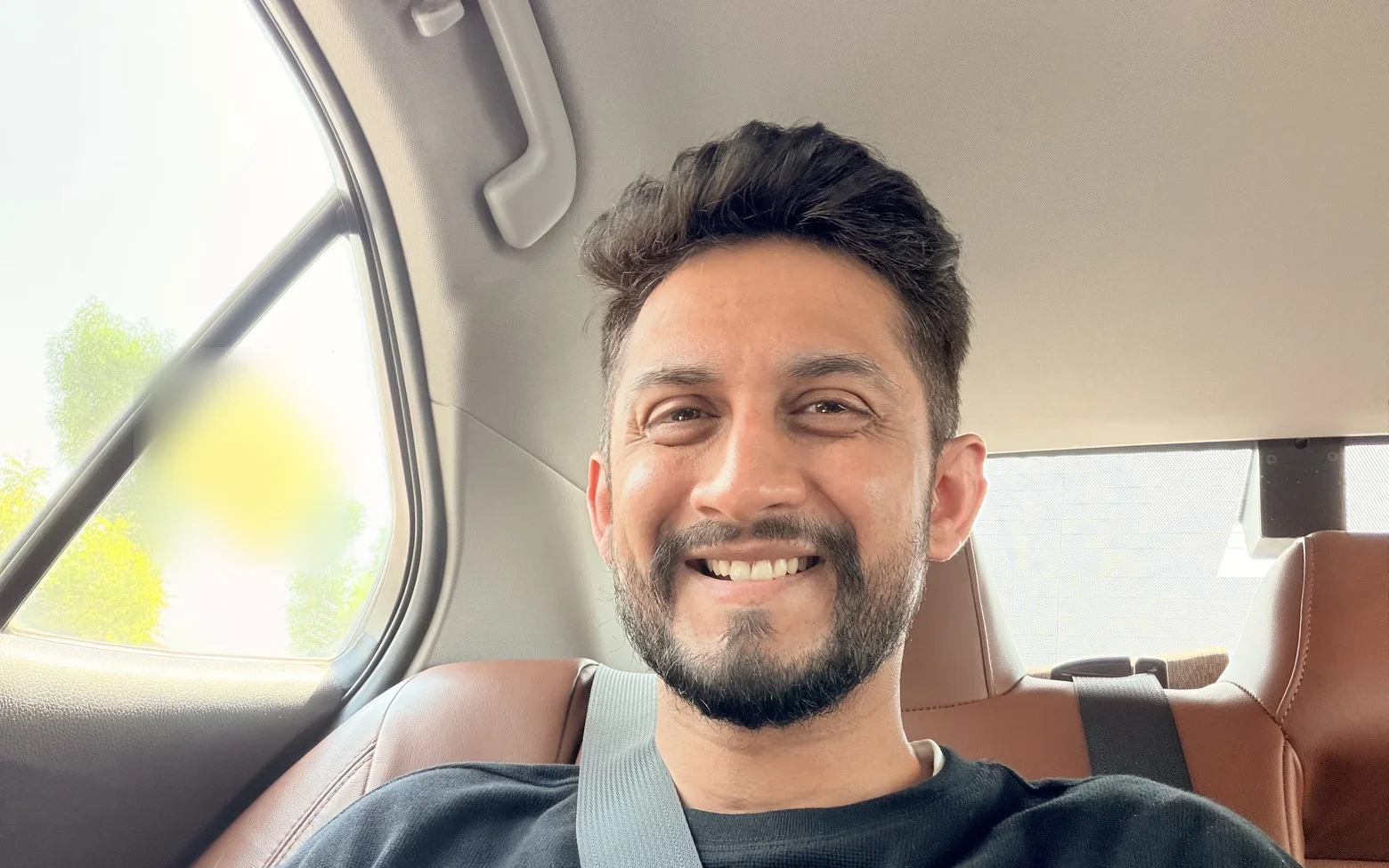 Digital Pratik smiling widely in the back seat of a car