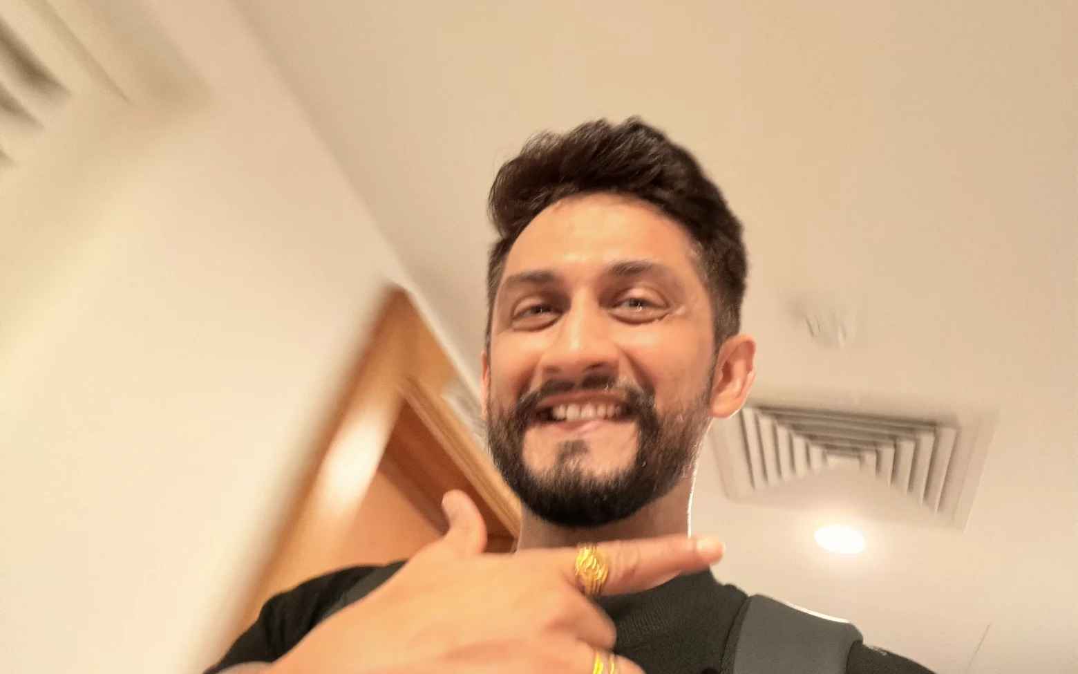 Digital Pratik grinning in a selfie and pointing at himself, a backpack strap on his shoulder