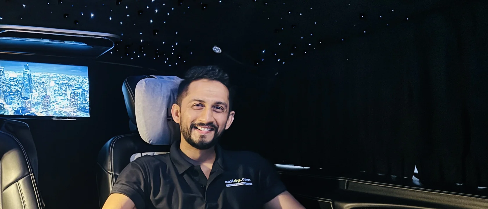 Digital Pratik smiling in the back seat of a van at night, in a black calldp.com polo
