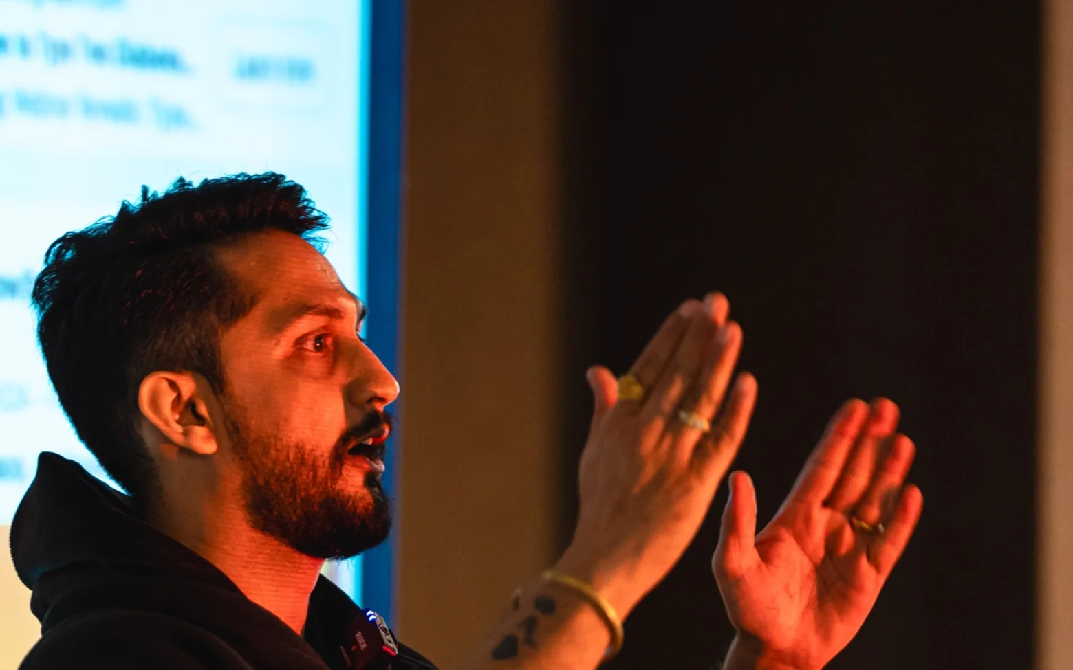 Digital Pratik speaking on stage in a dark hoodie, both hands raised as he talks