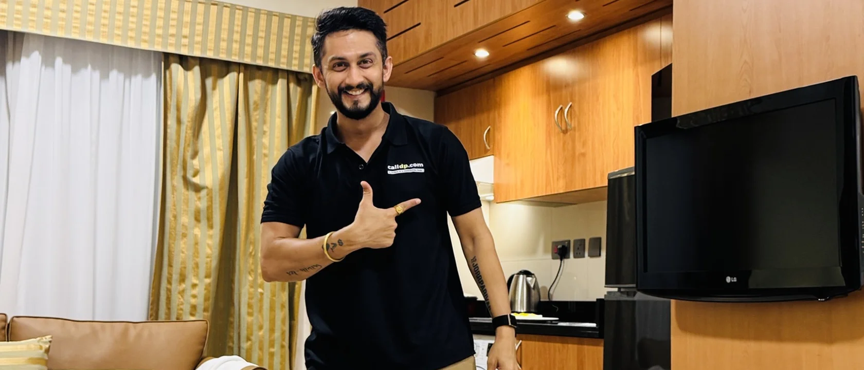 Digital Pratik smiling and pointing at the camera in a black polo shirt, standing in a living room