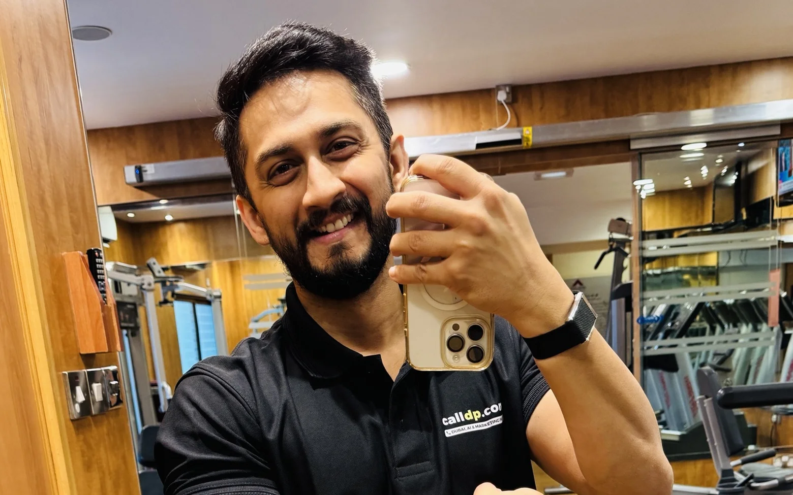 Digital Pratik smiling as he takes a mirror selfie with his phone in a gym