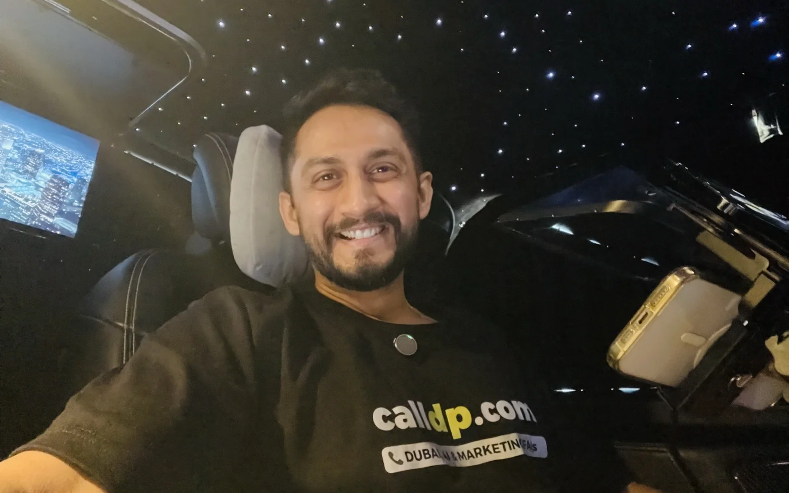 Digital Pratik smiling in a selfie in the back of a car at night, wearing a black calldp.com t shirt