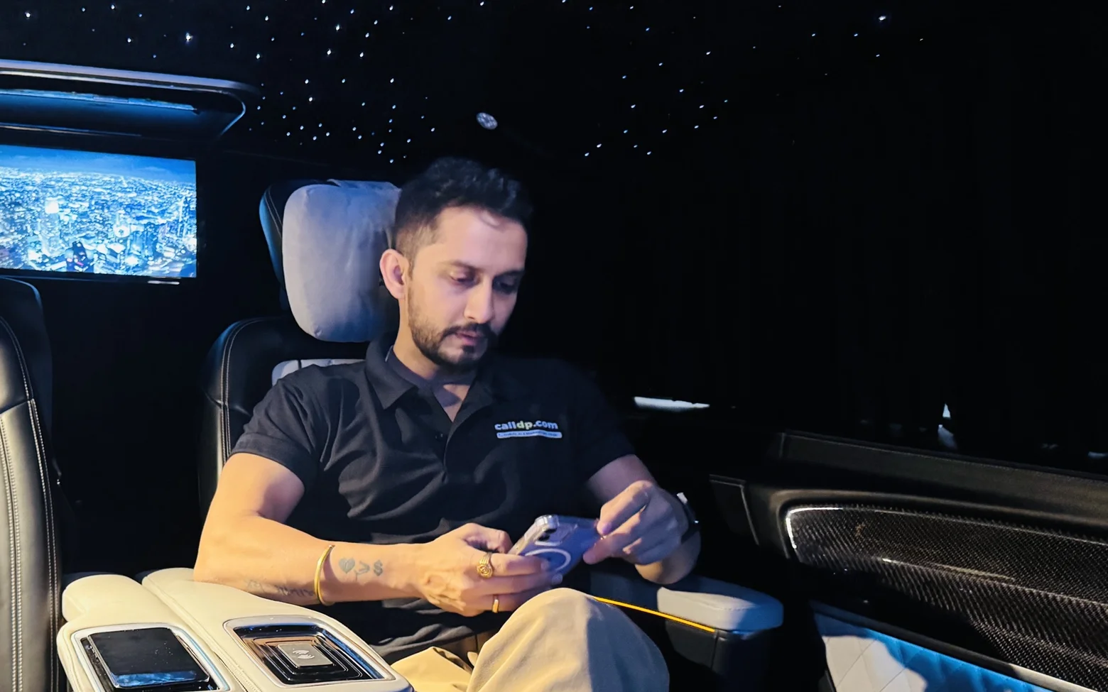 Digital Pratik in the back seat of a van at night, looking down at his phone in both hands