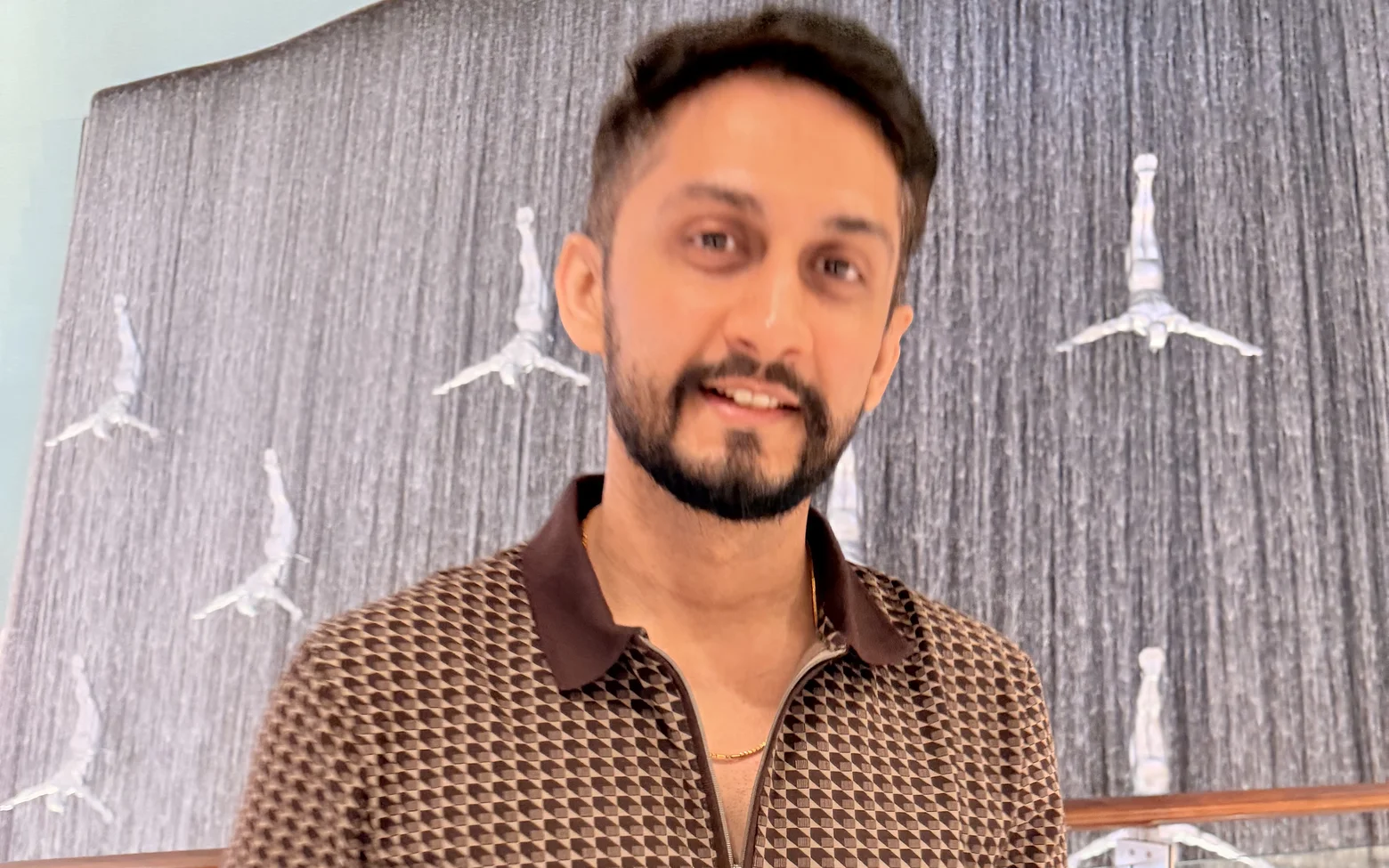 Digital Pratik smiling in a brown polo shirt in front of a tall indoor waterfall wall