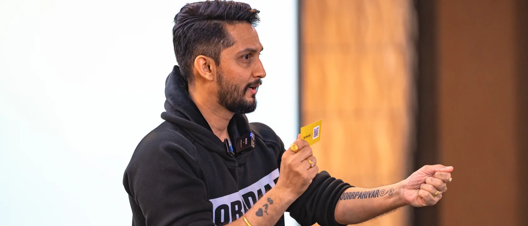 Digital Pratik in a black JorrDaar hoodie, speaking to a room with a small card in his hand