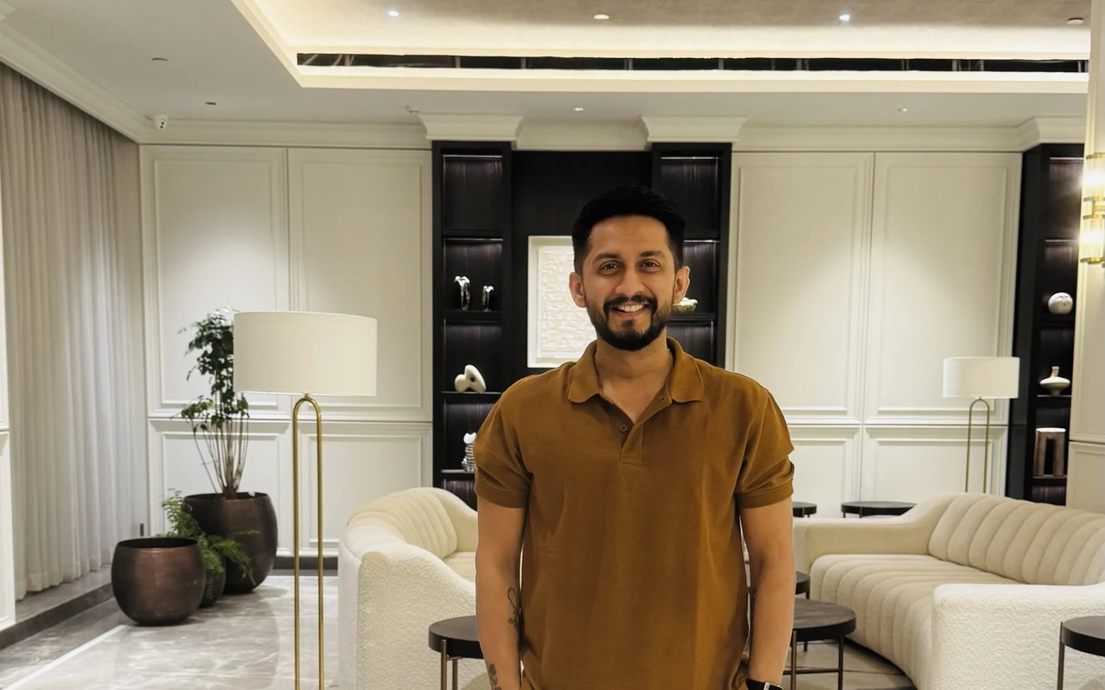 Digital Pratik smiling in a hotel lobby in a brown polo shirt, hands in his pockets