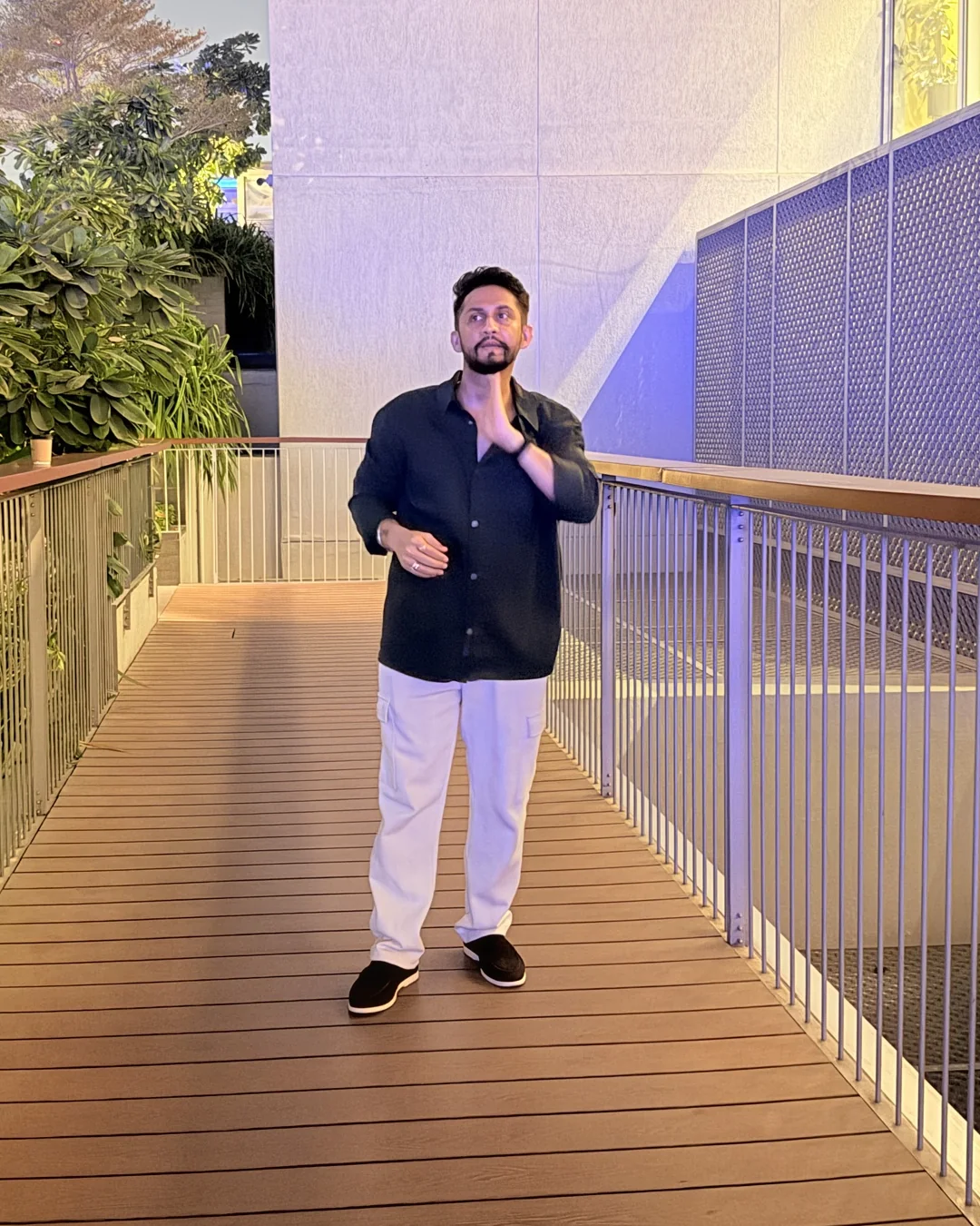 Digital Pratik smiling on a wooden walkway in Dubai at dusk, a tall tower behind him