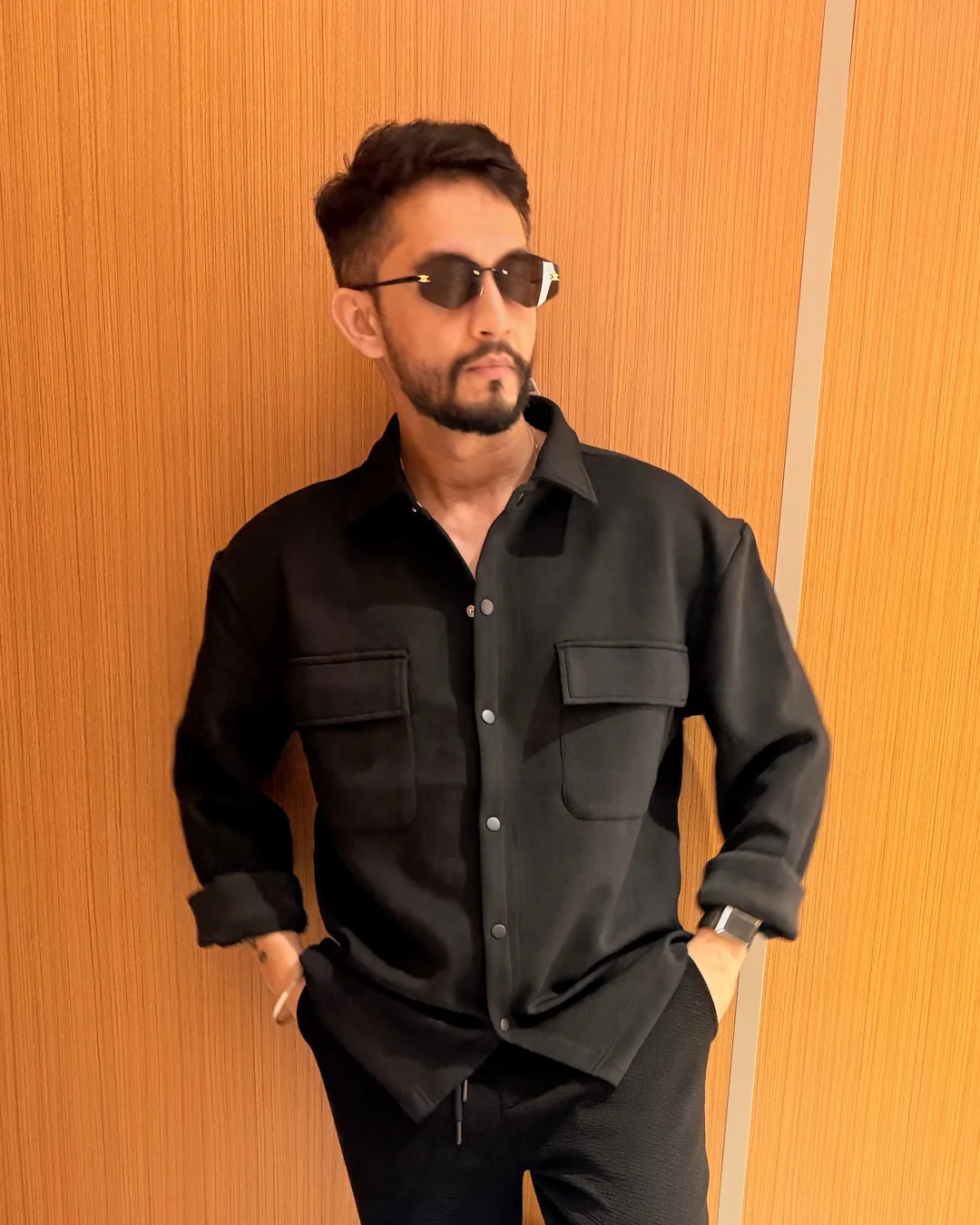 Digital Pratik in dark glasses, leaning on a wooden wall