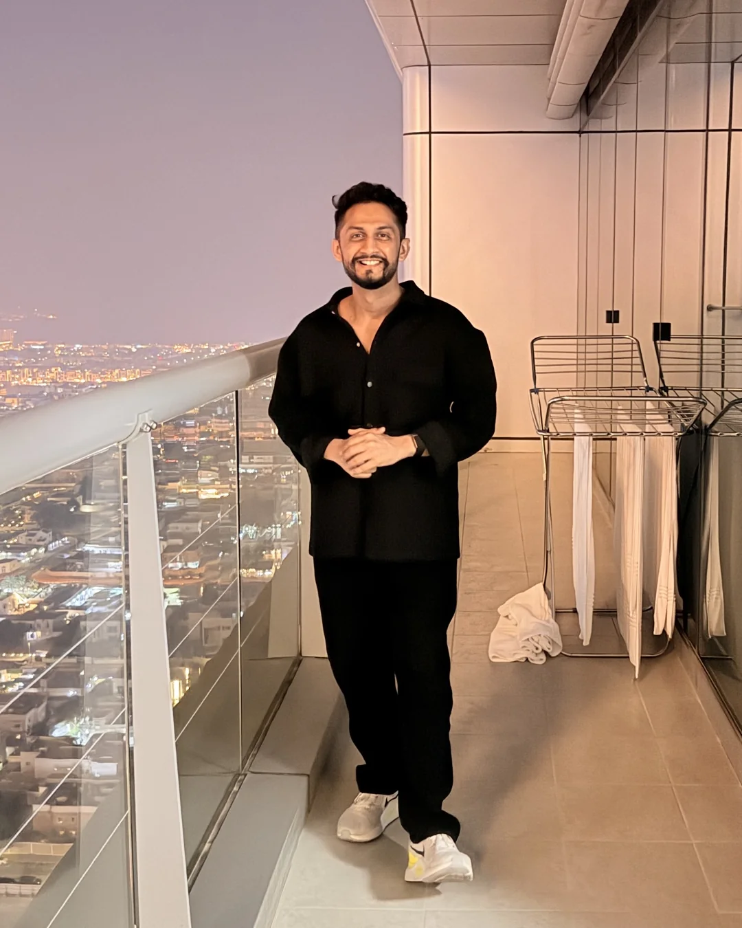 Digital Pratik smiling on a high balcony, the city lights below