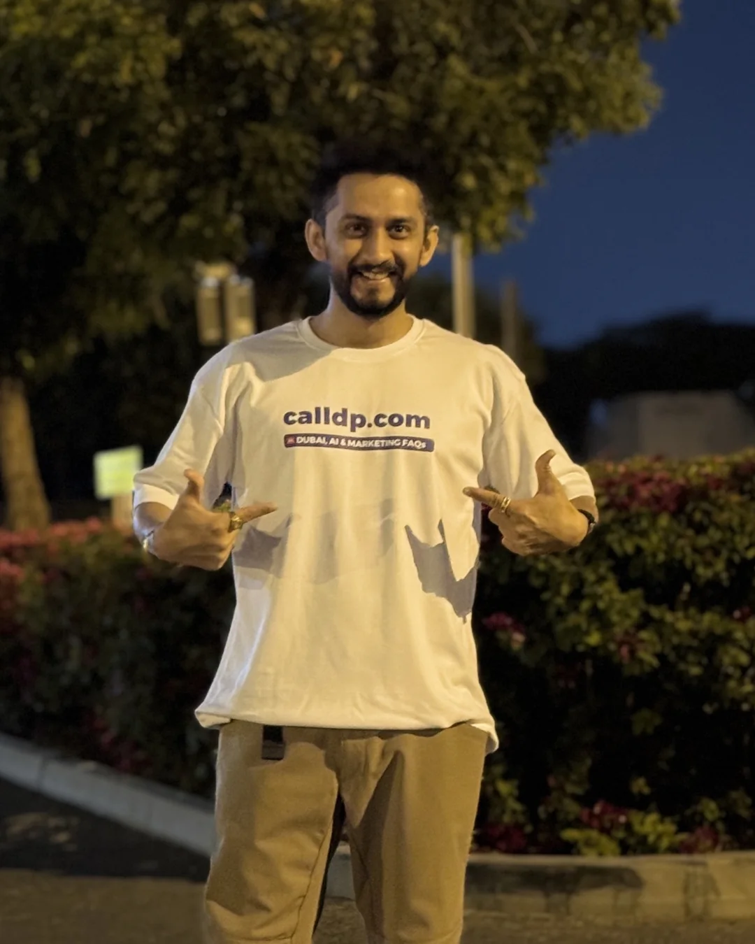 Digital Pratik smiling at night, pointing at the calldp.com line on his t-shirt