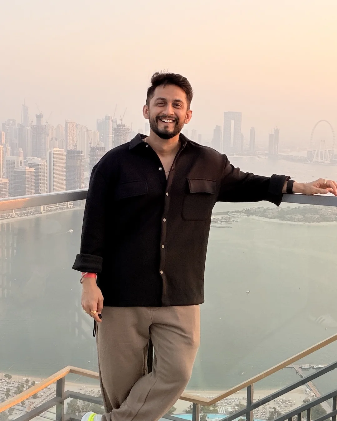 Digital Pratik smiling on a high deck at sunset, the Dubai Marina skyline behind him