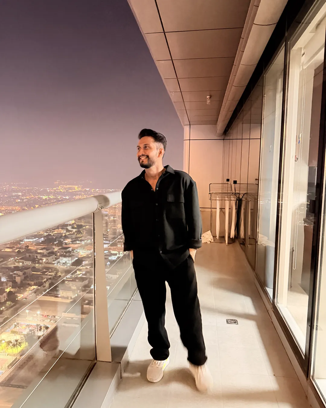Digital Pratik on a high balcony at night, the city lit up below
