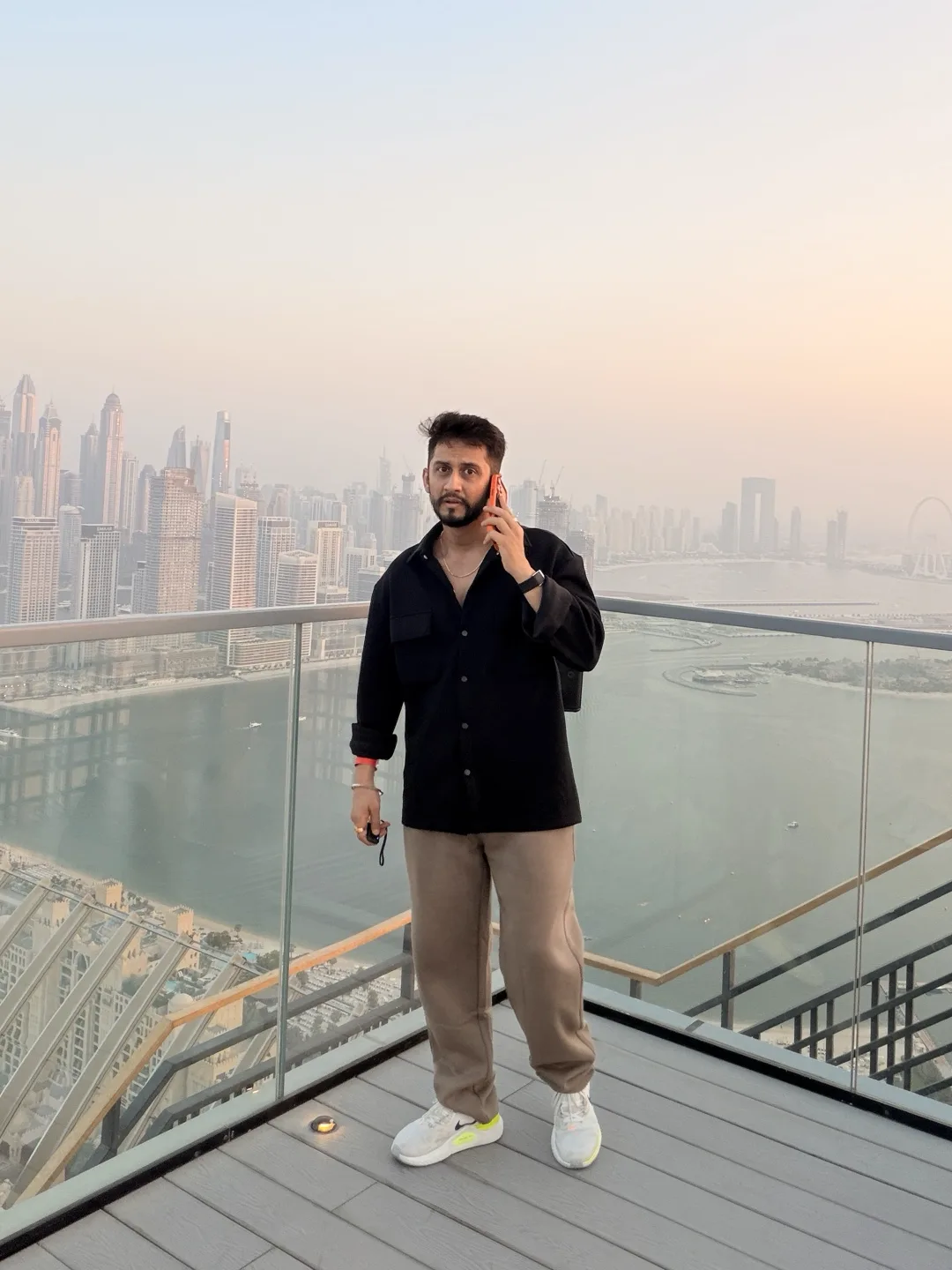 Digital Pratik on a phone call on a rooftop deck in Dubai, looking into the camera, the city behind him
