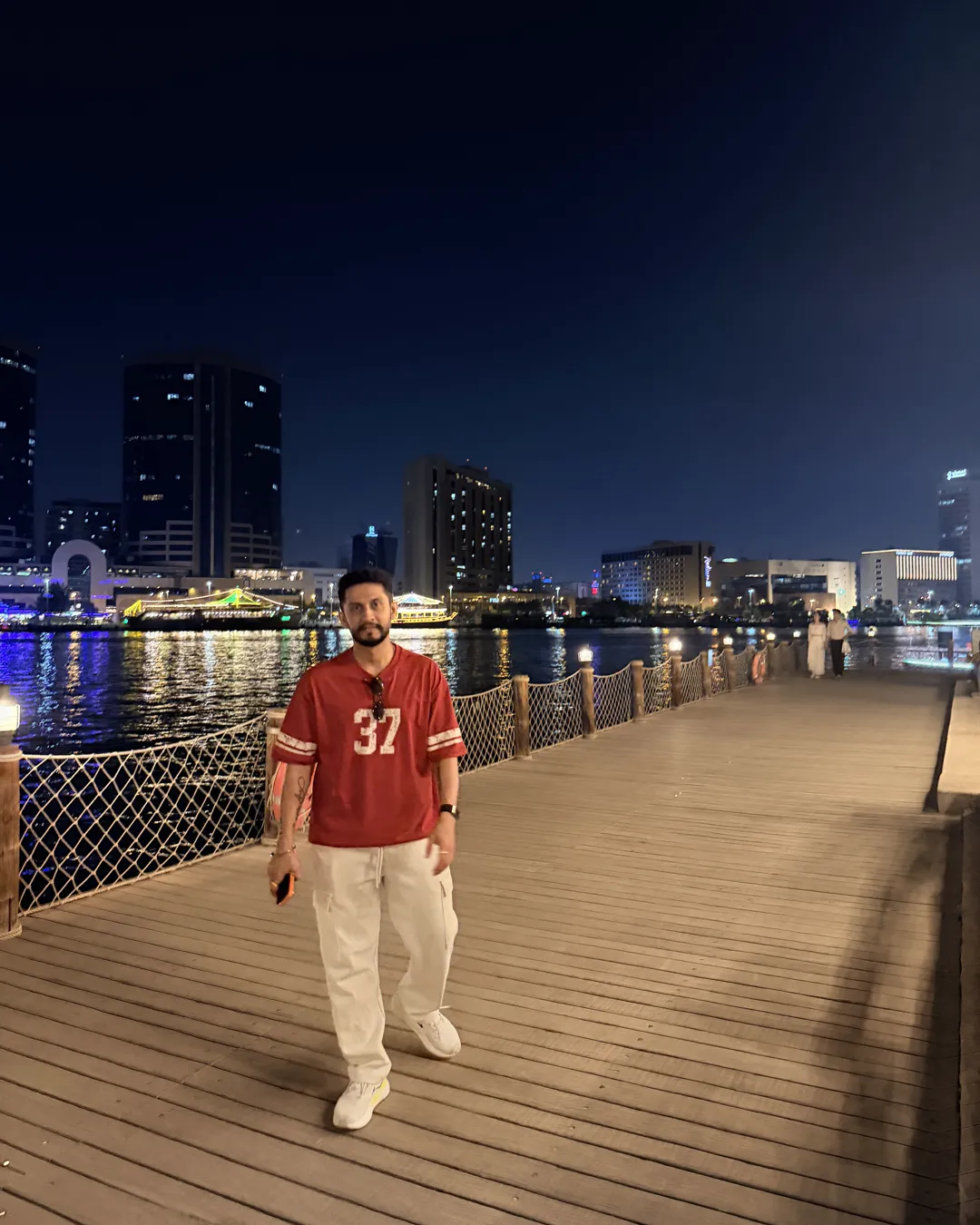 Digital Pratik on a boardwalk at night, the city lit up behind him